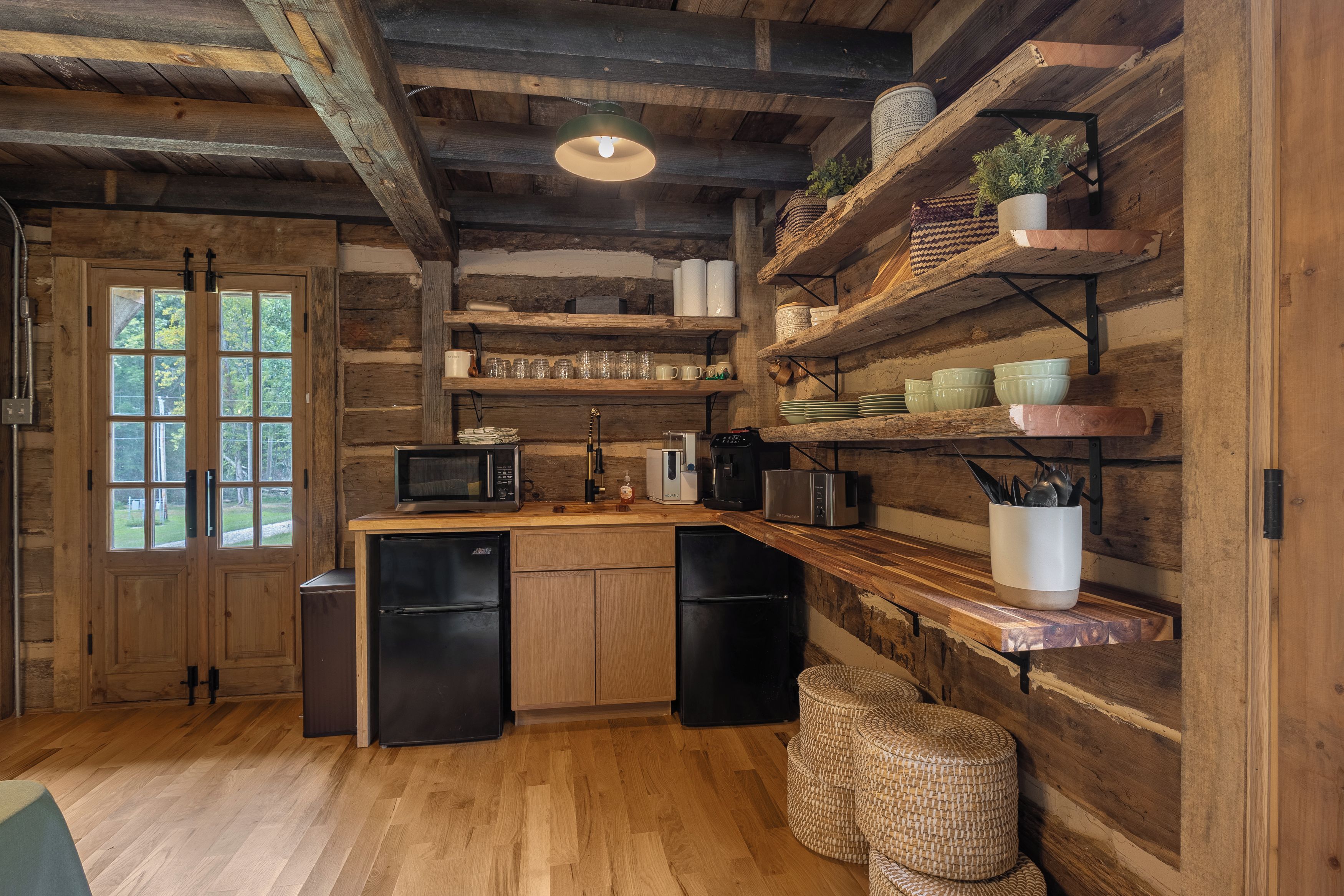 A rustic kitchen with wooden beams, a wooden countertop, and built-in shelves with kitchenware.