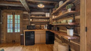 A rustic kitchen with wooden beams, a wooden countertop, and built-in shelves with kitchenware.
