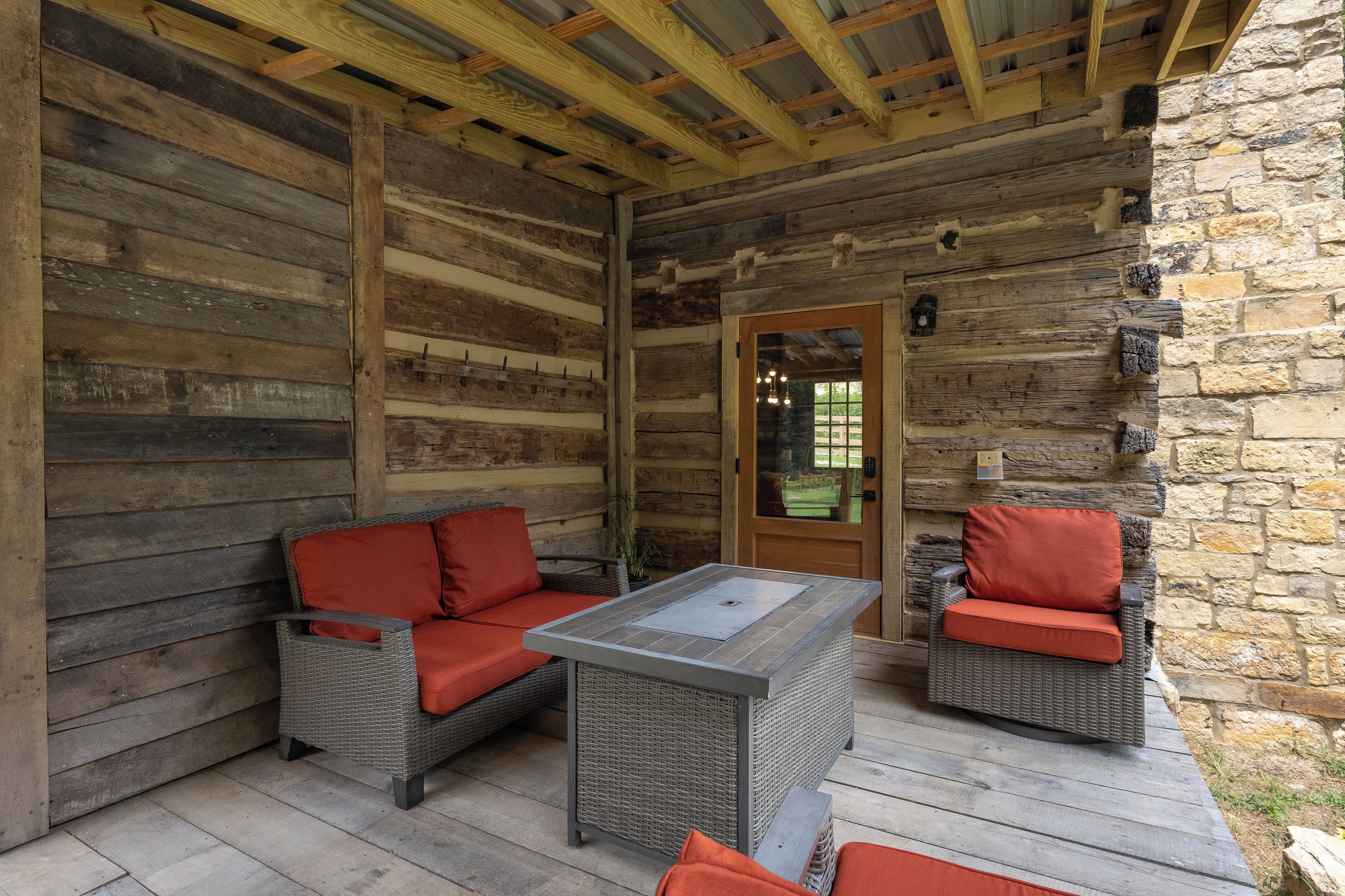 A log cabin with a stone wall, a wooden ceiling, and a glass door.