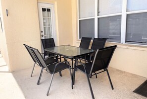 Eine Außenpatio mit einem Tisch aus Glas und vier Stühlen, einer Tür und einem Fenster mit Jalousien.