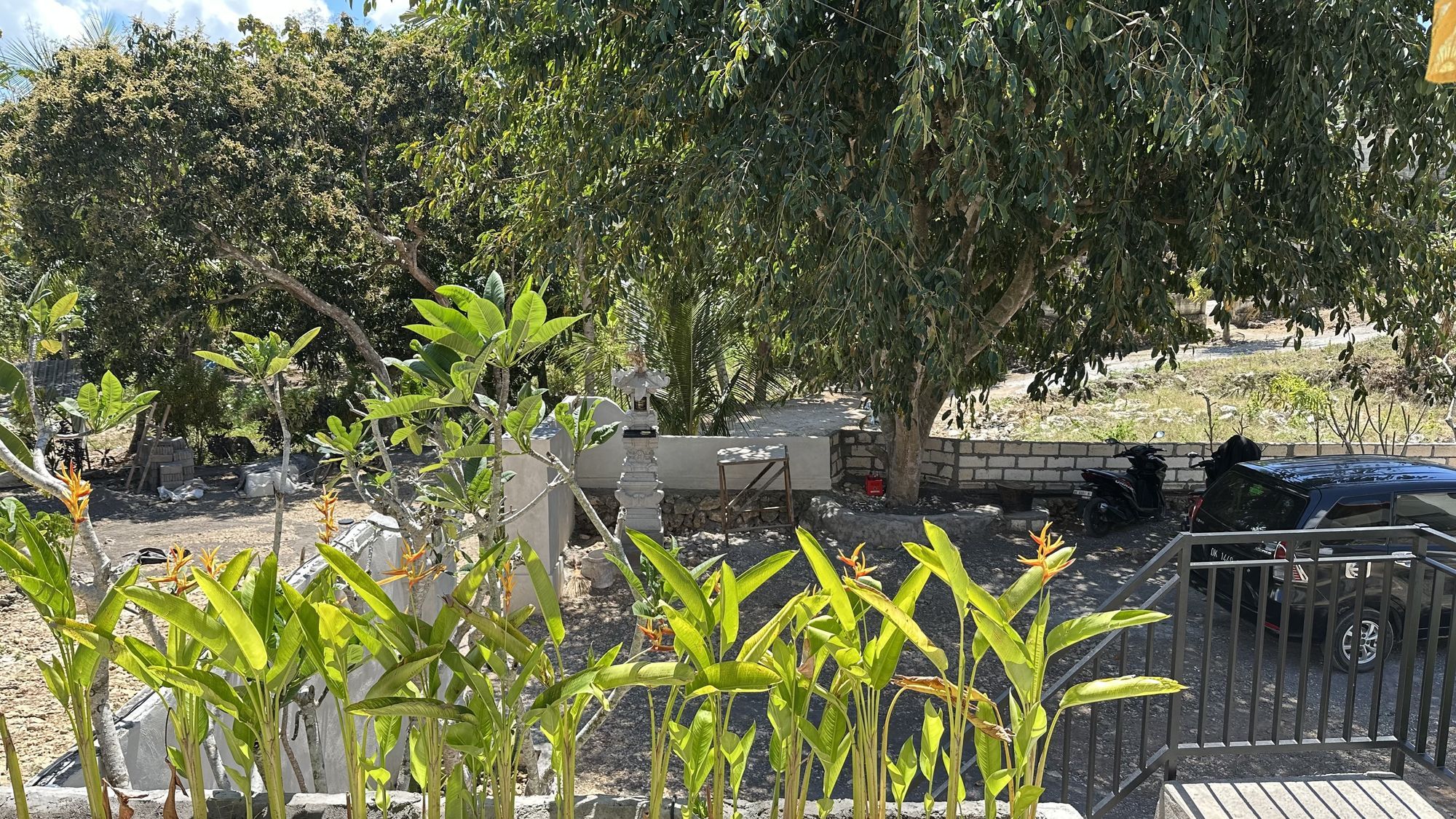 A garden area with various plants, a stone wall, and a parked vehicle.
