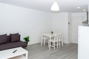 Ein modernes Wohnzimmer mit einem weißen Sofa, einem Esstisch mit Stühlen, einem weißen Couchtisch und einer Pendelleuchte.