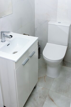 Un baño con un lavabo blanco, un inodoro y un cubo de basura.
