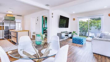Una sala de estar moderna con una mesa de centro de vidrio, sillas blancas, un reposapiés azul y un sofá gris.
