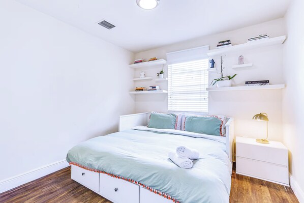 A bedroom with a bed, bedside tables, a nightstand, a lamp, and built-in shelving with books and decorative items.