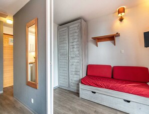 A room with a grey wall, a wooden door, a wardrobe, a red sofa, and a wall-mounted shelf. - Alpine Ski Apartment in Tignes for 4 (Tignes)
