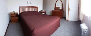 A bedroom with a bed, a dresser, a nightstand, a mirror, and a radiator. - Asure Colonial Court Motel and Conference Centre (Palmerston North)