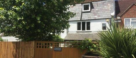 A two-story cottage with a visible window and a wooden fence.