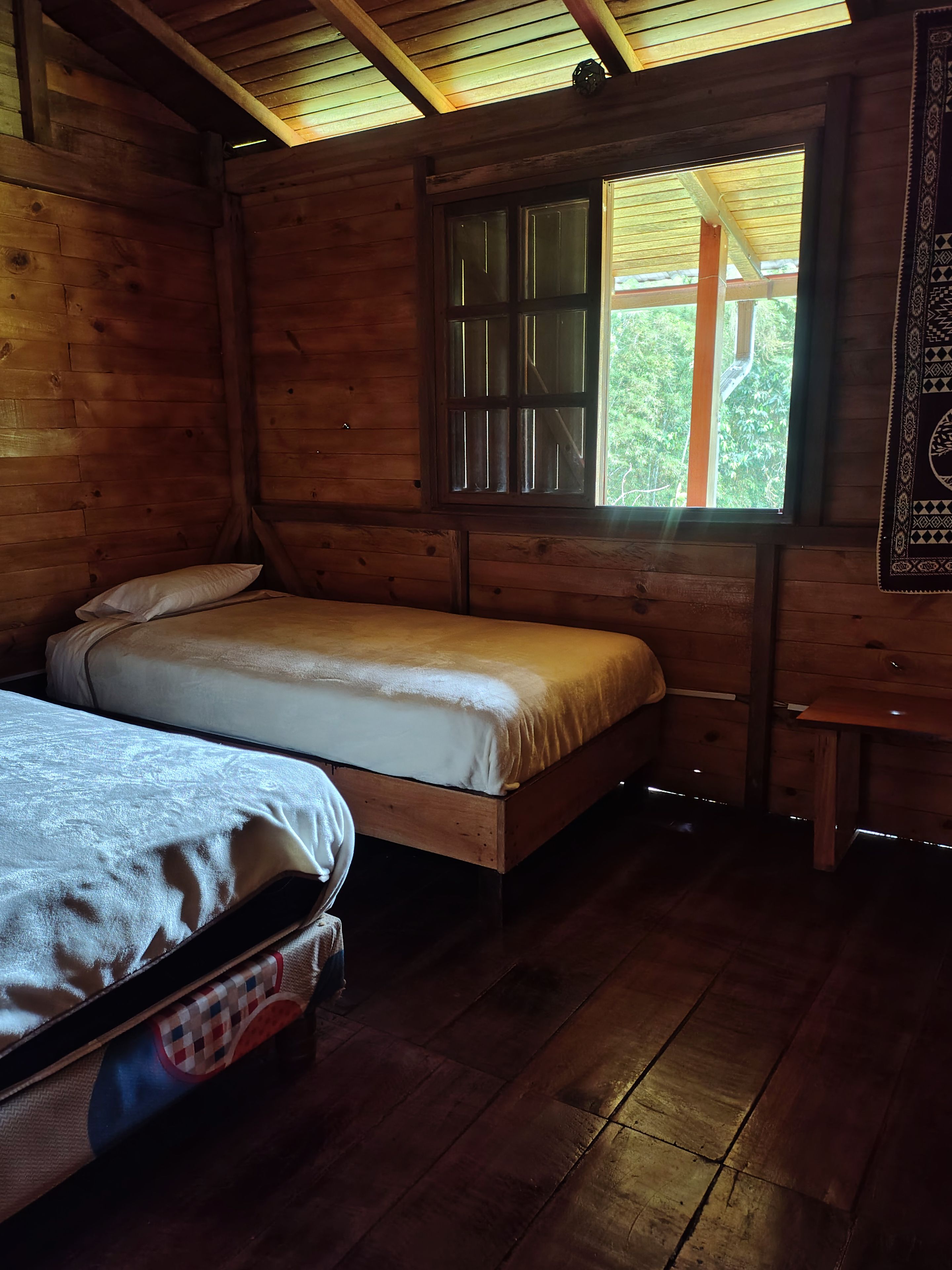 A wooden cabin room with two beds, a window, and a bench.
