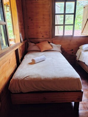 Una habitación tipo cabaña de madera con una cama individual, una ventana y una puerta.