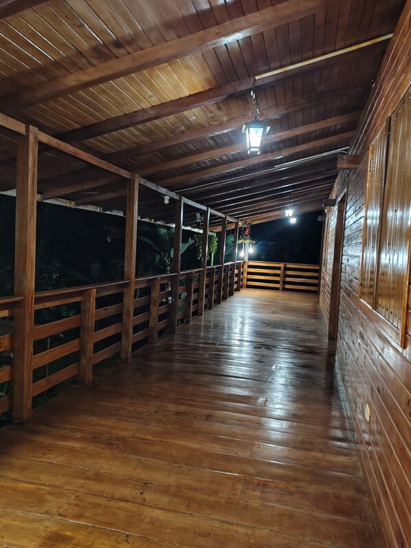 Una terraza cubierta de madera con barandillas, piso de madera y una lámpara colgante.