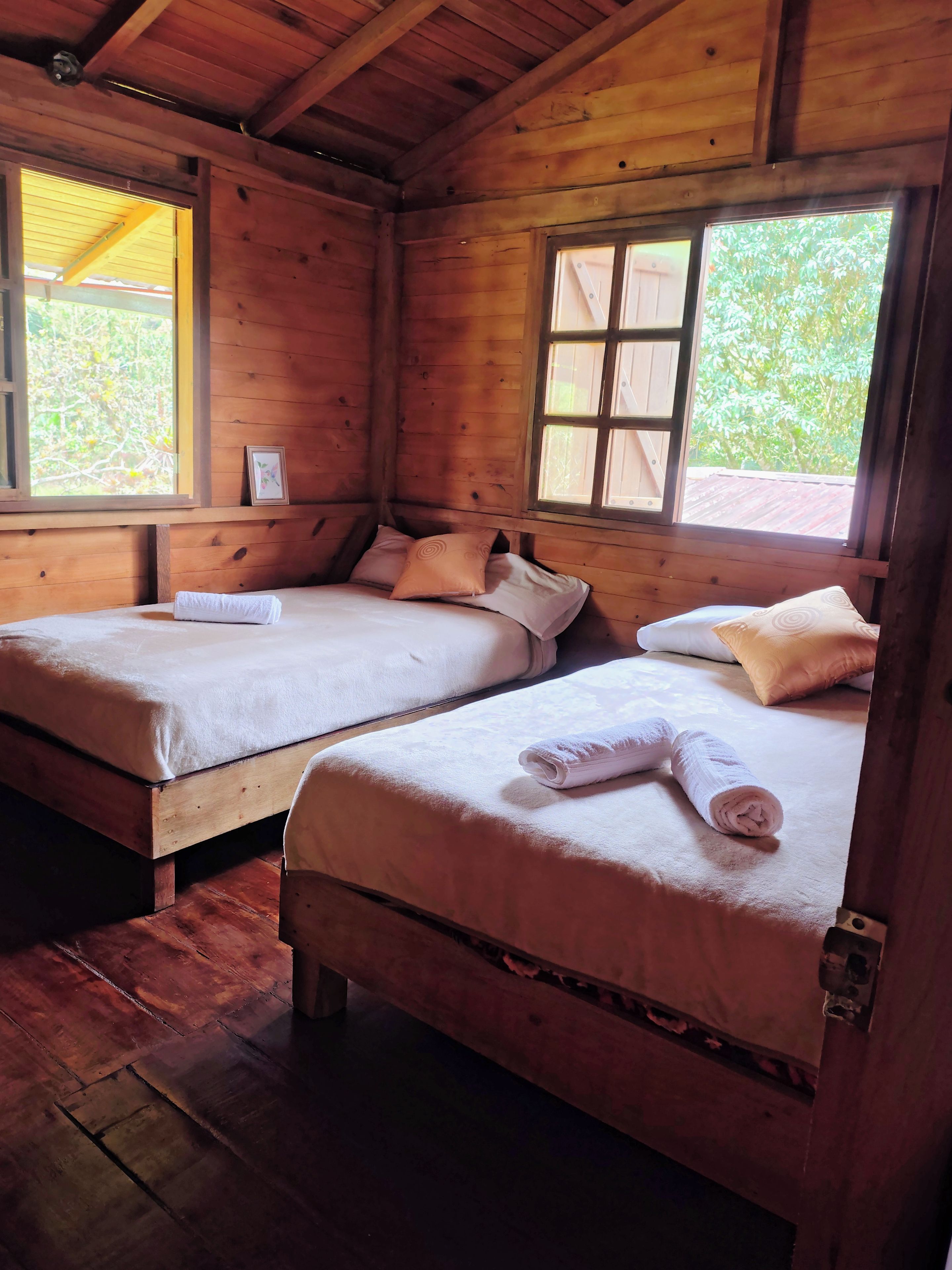Ein Zimmer in einer Holzhütte mit zwei Betten, jedes mit einem Kopfkissen und einem zusammengerollten Handtuch.