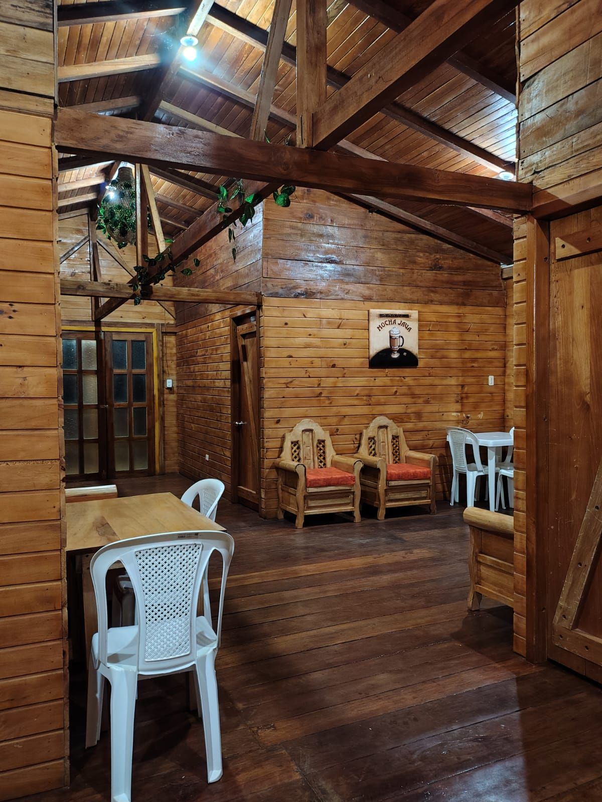 Ein Holzinterieur mit hoher Decke, Holzbalken, einem Holztisch mit Stühlen und einem Schild mit dem Bild einer Person.