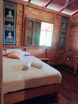 Una habitación tipo cabaña de madera con una cama, un ventanal y dos tapices en las paredes.