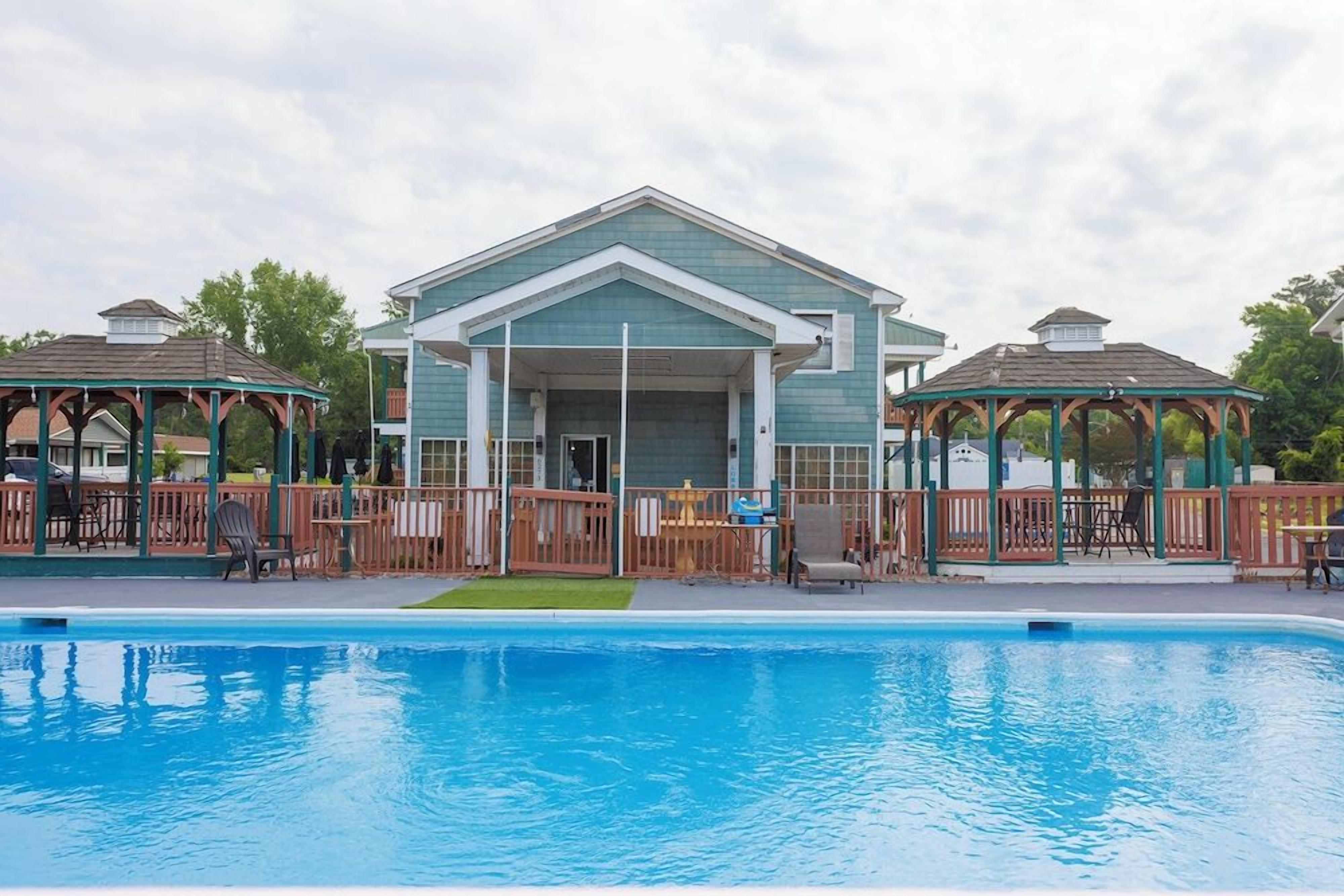 A swimming pool area with a building and two gazebos.