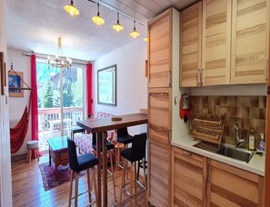 Eine gemütliche Küche mit Holzschränken, ein Essbereich mit Tisch und Stühlen und ein Blick ins Freie durch ein großes Fenster.