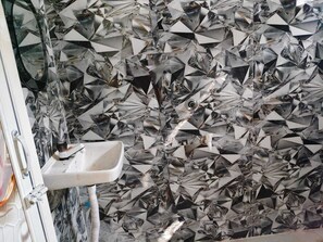 A bathroom with a sink and a wall covered in reflective, geometric tiles. - Deluxe Raj Guest House (Barakpur)