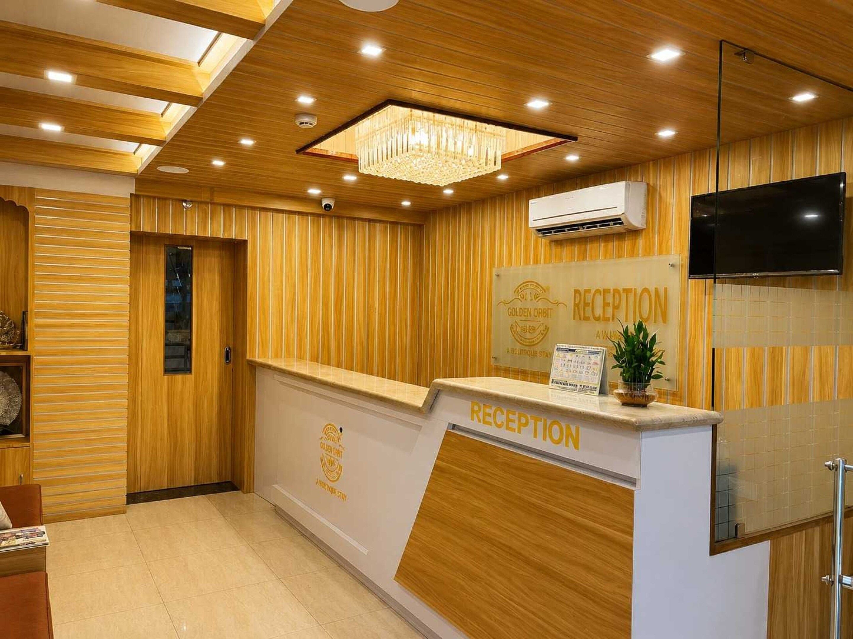 Zona de recepción con un panel de madera, mostrador de recepción, candelabro y televisor montado.