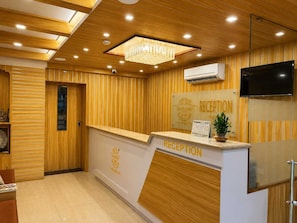 A reception area with a wooden panel wall, a reception desk, a chandelier, and a mounted television. - Deluxe Raj Guest House (Barakpur)
