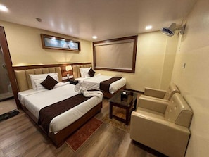 A hotel room with two beds, a sofa, a small table, and a ceiling fan. - Deluxe Raj Guest House (Barakpur)