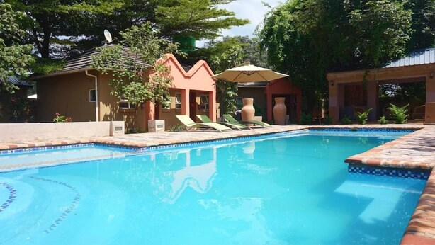 Una piscina con sillas de descanso y sombrillas, rodeada de edificios y árboles.