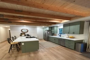 A modern kitchen with wooden beams, a central island, and green cabinetry.