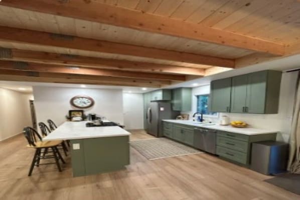A modern kitchen with wooden beams, a central island, and green cabinetry.