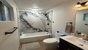 Une salle de bain avec un mur en marbre, une baignoire, des toilettes et un lavabo avec un miroir.
