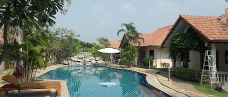 Ein Swimmingpool mit gefliesten Rändern, umgeben von Palmen und einem Gebäude mit einem Ziegeldach.
