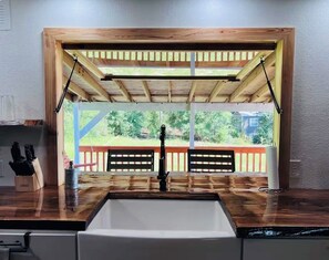 Une cuisine dotée d’un évier encastré, d’un plan de travail en bois et offrant une vue sur le jardin arrière par une fenêtre.