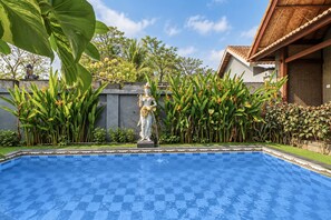 A swimming pool with a statue in the center, surrounded by lush greenery and a building with a tiled roof. - Belvilla The Cemok Cottage  (Penida Island)