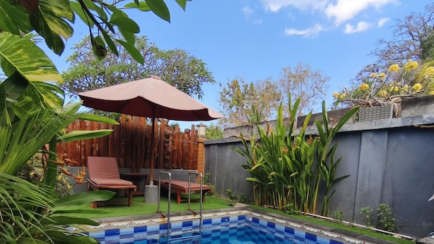A swimming pool with a checkered tile pattern, surrounded by a wooden fence, with a patio area featuring a table and chairs.