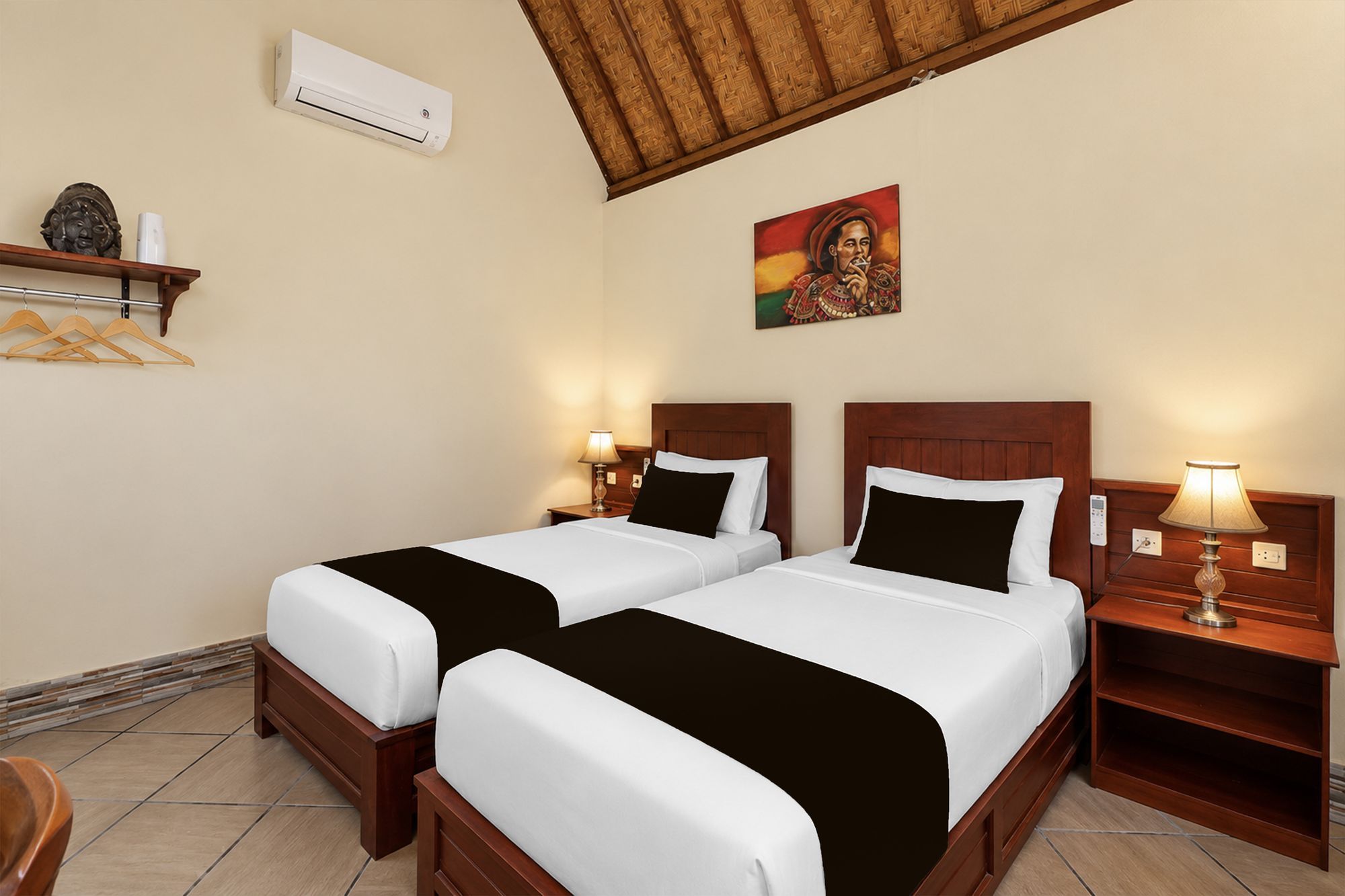 Habitación de hotel con dos camas, aire acondicionado de pared, un cuadro y una estantería con un objeto decorativo.