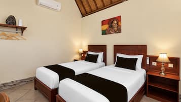 Habitación de hotel con dos camas, aire acondicionado de pared, un cuadro y una estantería con un objeto decorativo.