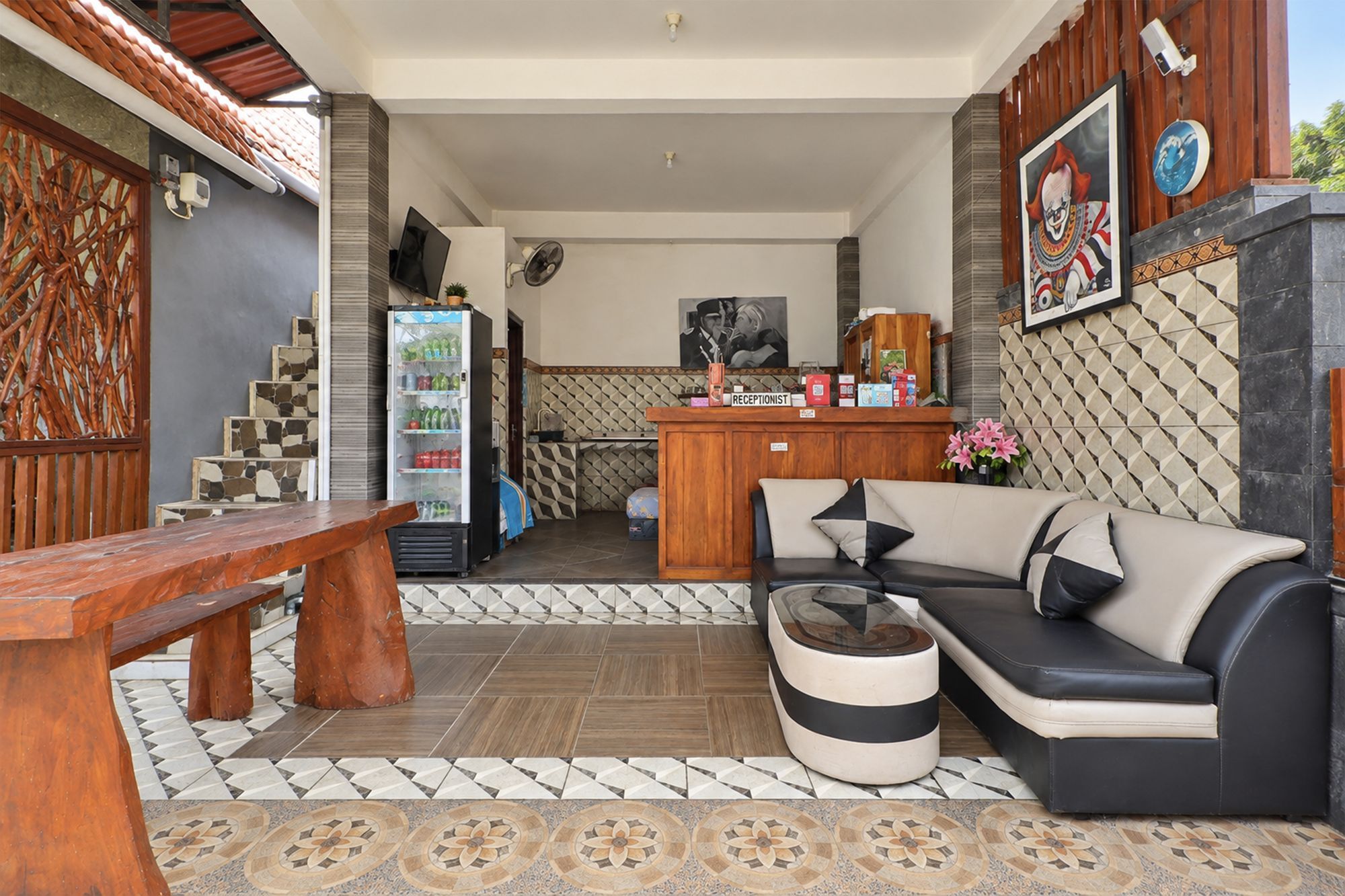 Un área de recepción con un sofá, un banco, un refrigerador y piso de baldosas.