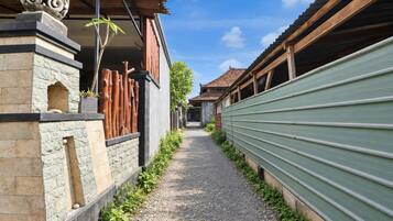 Un estrecho callejón con un camino de grava, flanqueado por edificios con fachadas de piedra y madera, y una cerca de metal verde en un lado.
