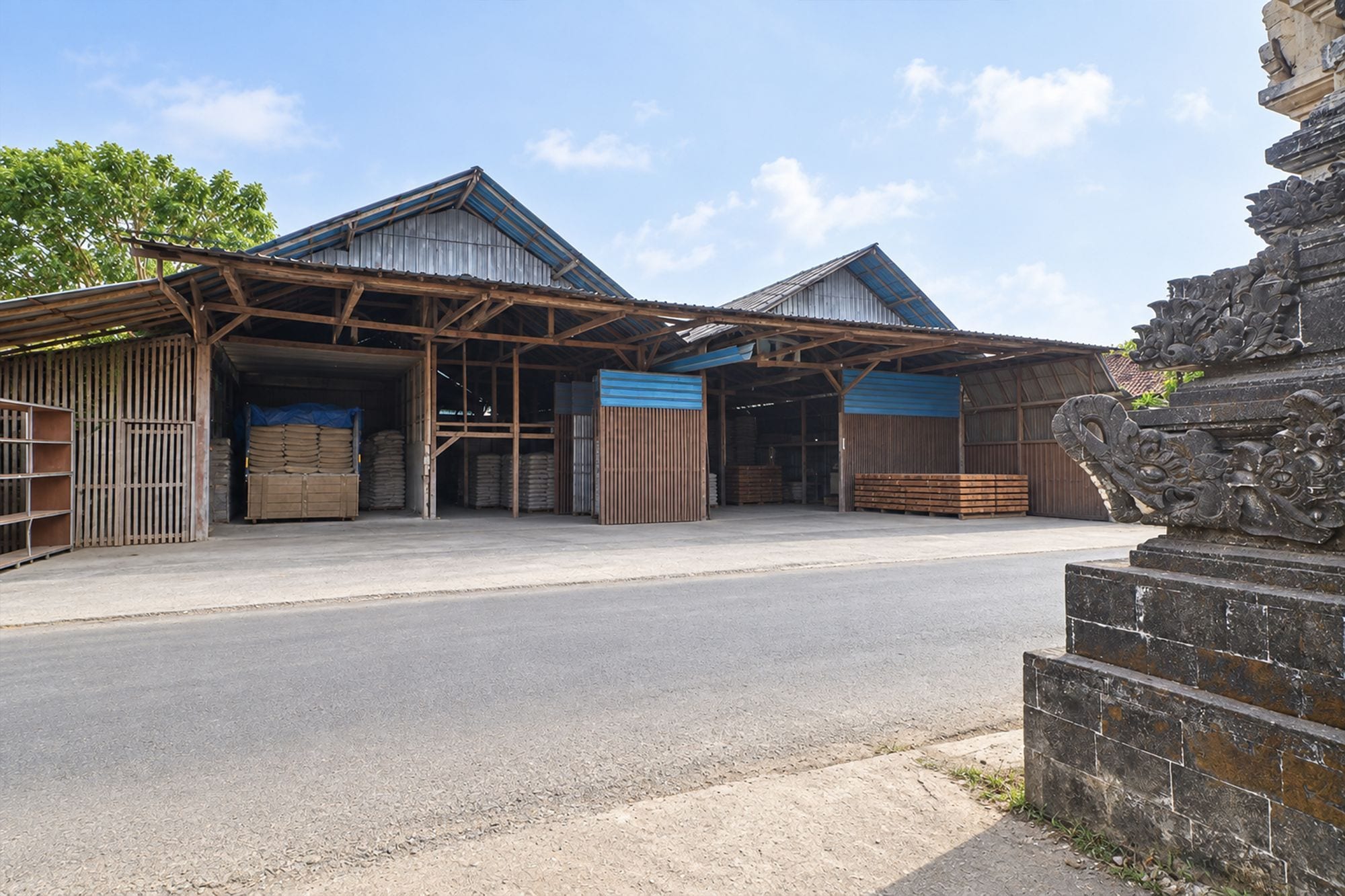 A warehouse with open-sided metal sheds, a paved entrance, and a stone structure with carvings.