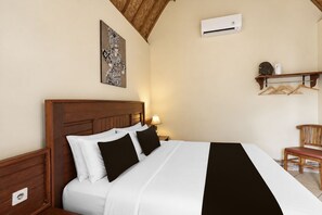 A hotel room with a wooden headboard, a bed with white and black bedding, a wall-mounted air conditioner, a bedside lamp, and a wooden chair. - Belvilla The Cemok Cottage  (Penida Island)