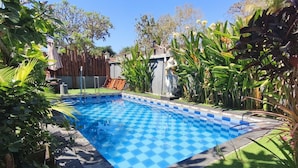 A swimming pool with a checkered pattern, surrounded by lush greenery and a wooden fence.