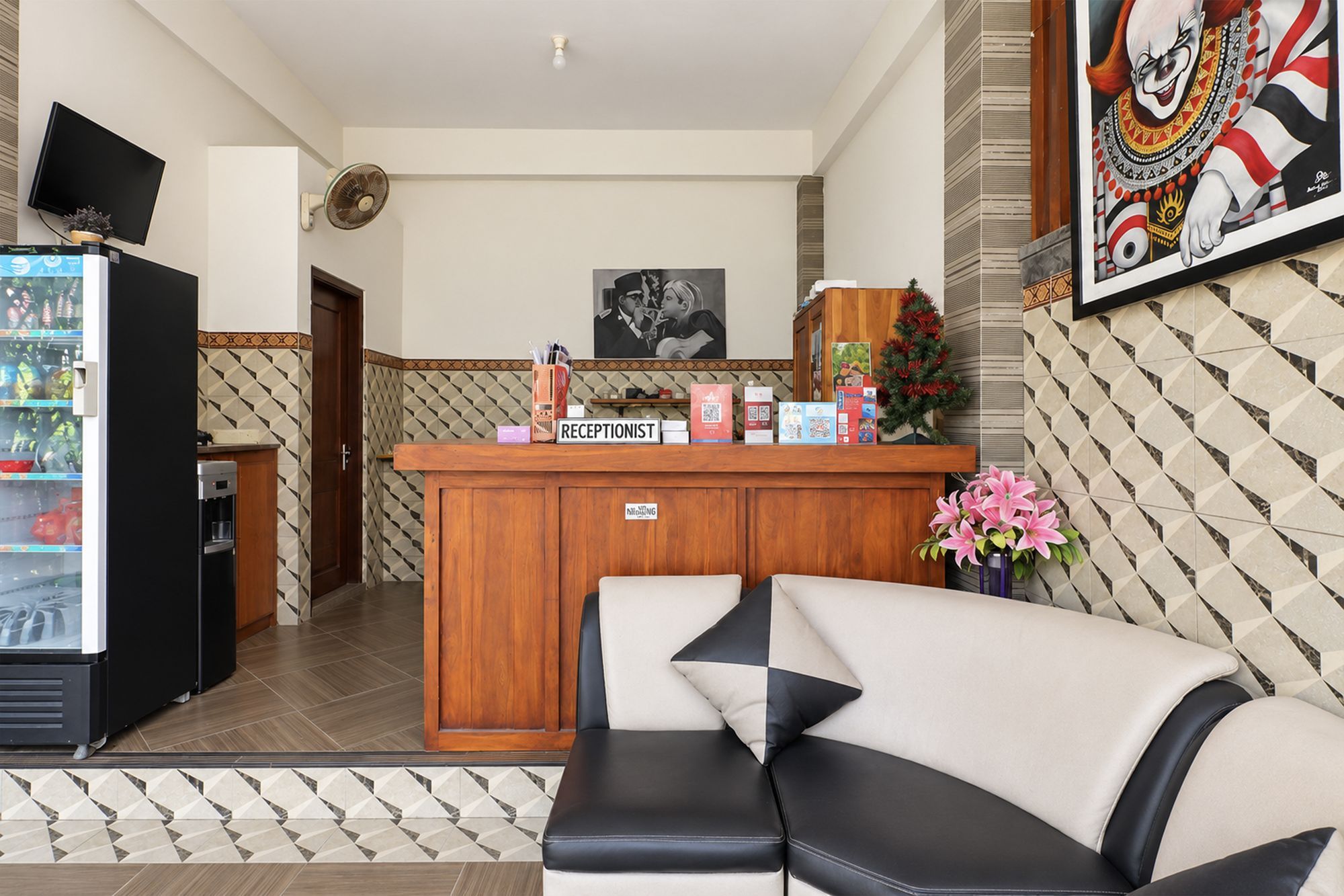 Una zona de recepción con mostrador de madera, un sofá, un refrigerador y un televisor montado en la pared.
