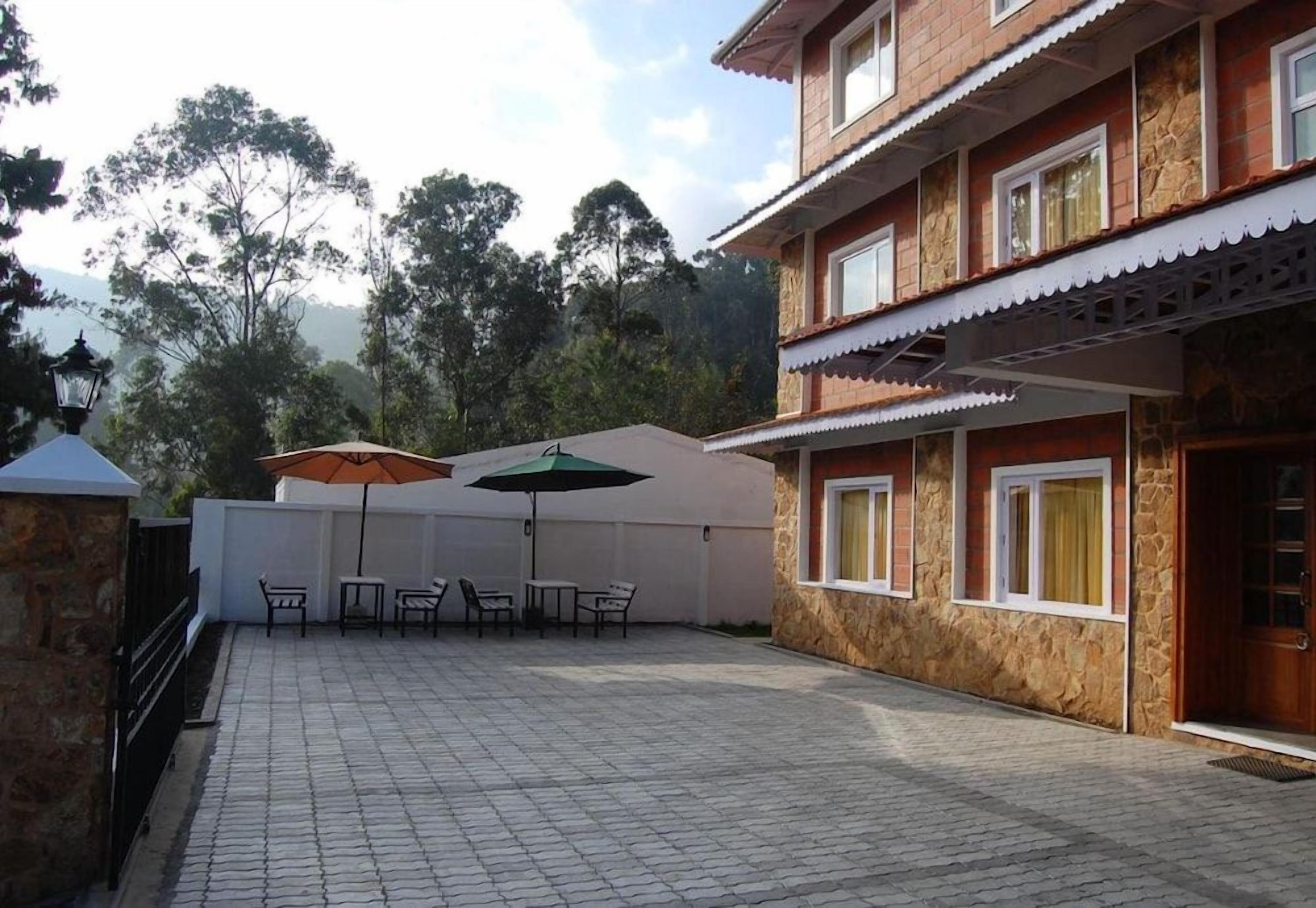 A building with a stone facade, multiple windows, and a paved patio area with outdoor furniture and umbrellas.