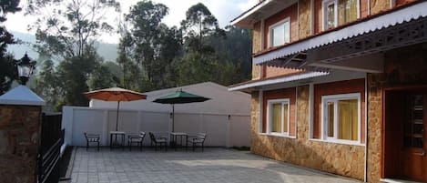 A building with a stone facade, multiple windows, and a paved patio area with outdoor furniture and umbrellas.