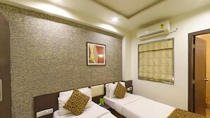 A hotel room with two beds, a textured wall, a framed picture, an air conditioning unit, and a window with a curtain. - OYO Rooms Kanak Road (Rajkot)