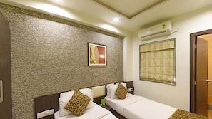 A hotel room with two beds, a textured wall, a framed picture, an air conditioning unit, and a window with a curtain. - OYO Rooms Kanak Road (Rajkot)
