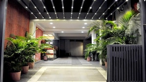 A corridor with potted plants, a tiled floor, and a modern ceiling design. - OYO Rooms Kanak Road (Rajkot)