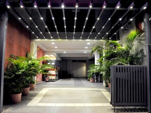 A corridor with potted plants, a tiled floor, and a modern ceiling design. - OYO Rooms Kanak Road (Rajkot)