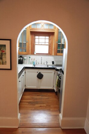 A kitchen with white cabinets, a black countertop, and a window above the sink. - Little Five Points Lodge | Walkable 1BR + Hot Tub (Atlanta)