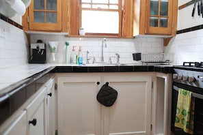 A kitchen with white cabinets, a black countertop, a stove, and a window above the sink. - Little Five Points Lodge | Walkable 1BR + Hot Tub (Atlanta)