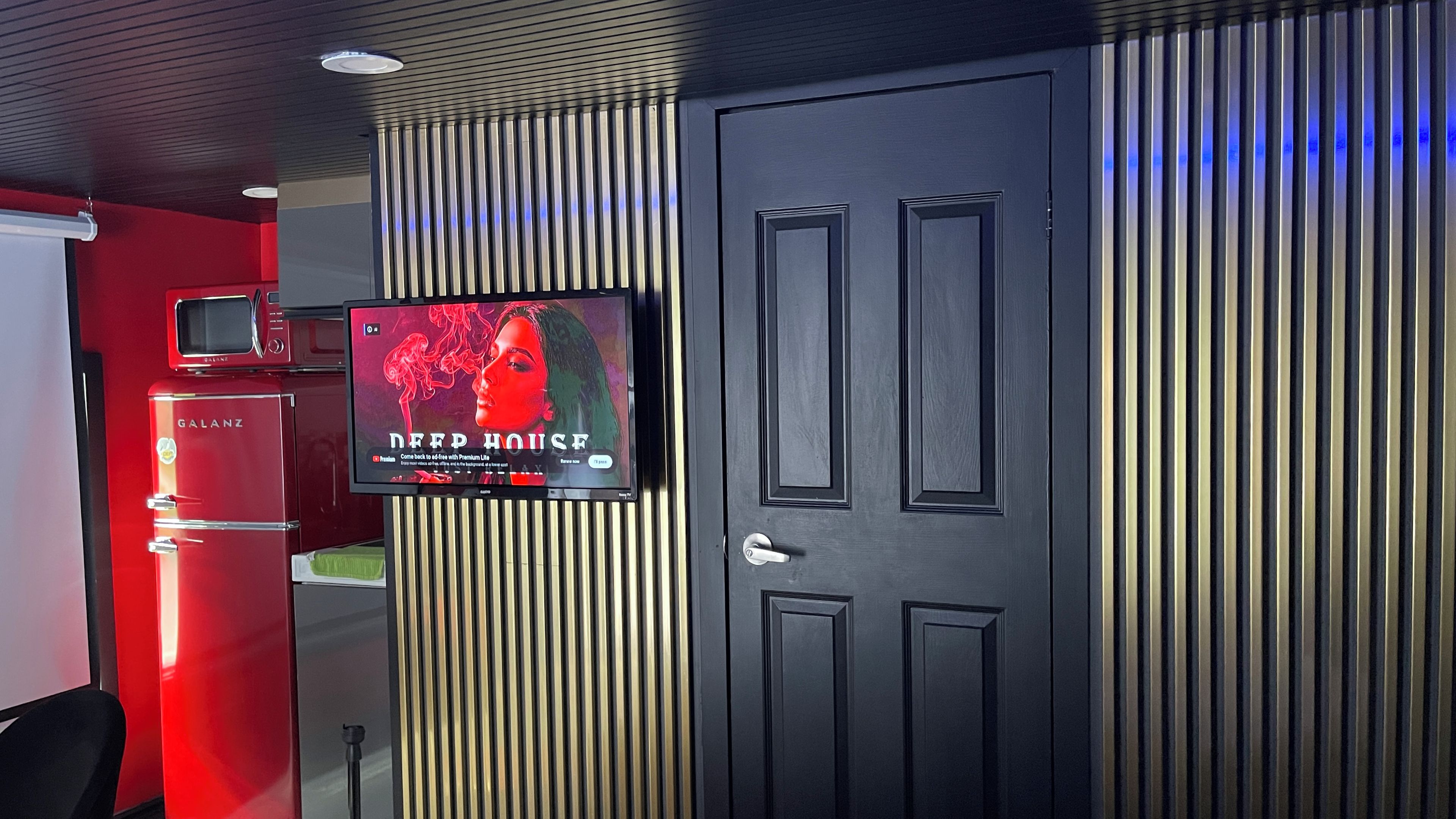 Ein Zimmer mit an der Wand montiertem Fernseher, einer Tür und einem roten Gerät.
