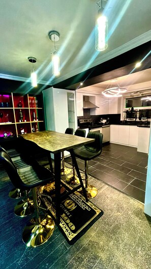 Une cuisine moderne avec un coin repas, comprenant une table avec des chaises, un bar avec des étagères et une cuisinière visible.